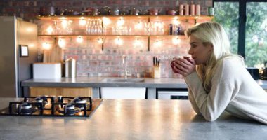 Kadın kırmızı seramik bardak kaldırıyor, mutfakta kameraya gülümserken kahveyi yudumluyor, fotokopi çekiyor. Mutfak, konforlu, yaşam tarzı, iç mekan, rahatlama, sıcaklık