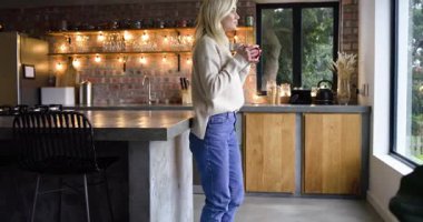 Mutfağa giren kadın elinde kırmızı kupayla beton adada dinleniyor. Kokusunu soluyor ve gülümsüyor. Rahat, rahatlama, sabah, evcil, yaşam tarzı, sıcak, dinginlik