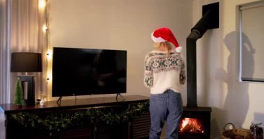 Odaya giren bir kadın konsolun üzerine süs kavanozu yerleştiriyor, bayram dekoru için hediyelerin etrafına kurdele bağlıyor. Şenlikli, rahat, kutlama, dekorasyon, mevsimlik, iç mekan, ortam