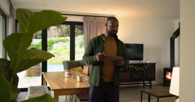 Afro-amerikan bir adamın tabletini aldıktan sonra, evdeki masaya doğru baktı, başını kaldırdı. Teknoloji, yaşam tarzı, modern, iç mekan, rahatlama, çalışma alanı, kentsel