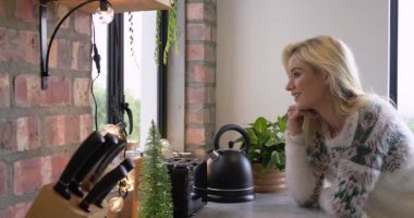 Tezgâha yaslanan kadın, sicim ışıkları altında kameraya gülümseyen, mekanı kopyalayan. Düşünce, konforlu, iç mekan, ortam, yaşam tarzı, minimalizm, sükunet