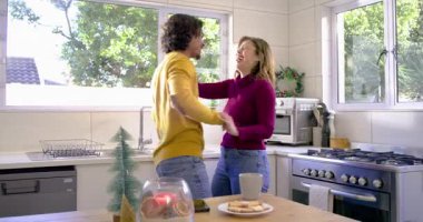 Elinde kahve fincanı olan kadına uzanan adam mutfak adasında dans eden çifti kabul ediyor. Romantizm, samimiyet, uyum, konfor, ev, etkinlik, bağlantı