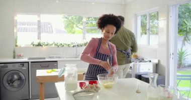 Buzdolabından süt taşıyan bir adam gibi adadaki kasede hamuru çırpan çiftten sonra. Modern mutfak, aşçılık, ev hayatı, taze malzemeler, aile aktiviteleri.