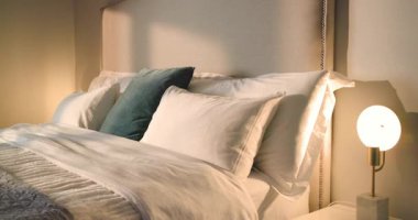 Güneş ışığı hareket eden gölgeler oluştururken kamera yastık düzenini ortaya çıkarmak için yataktan geri çekiliyor. Lüks, konfor, sükunet, zarafet, ev dekorasyonu, rahatlık, konfor.