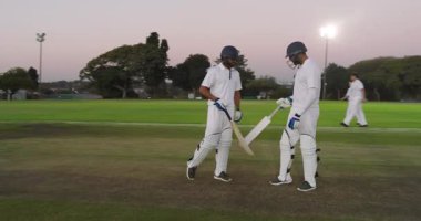 Vuruş seansından sonra saha dışına çıkan çeşitli erkek takım arkadaşları sopa vuruyor ve eldivenleri ayarlıyorlar. Kriket, takım arkadaşları, alacakaranlık, kutlama, sportmenlik, yoldaşlık, atletizm