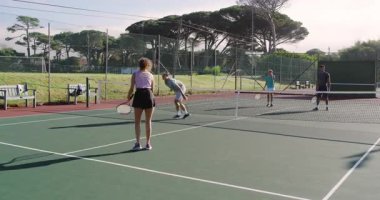 Asyalı adam topu yeşil sahada atıyor, çeşitli takımlar raketlerle yarışıyor, oyuna devam ediyor. Spor, atletizm, yarışma, boş zaman, açık hava, aktif giyim, fitness