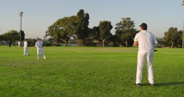 Çeşitli erkek takım arkadaşları kriket topunu serbest bırakıyor yarasaları kovalıyor, kepçeleme yapıyor, parkta yeniden toplanıyorlar. Atletik, takım çalışması, açık hava, eğlence, enerji, spor, eğlence
