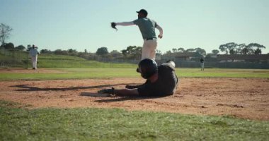 Vurucu dünyalıyı vuruyor, koşucu birinci kaleye dalıyor, erkek saha oyuncuları ilk kalede oynuyorlar. Atletizm, takım çalışması, aksiyon, spor, açık hava, rekabet, hareket