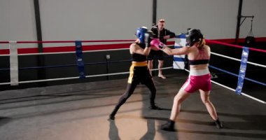 Antrenörde bayan boksörler ringde başlık ve eldiven keskinleştirme becerileri ile yumruk yumruğa dövüşüyorlar. Atletik, rekabet, antrenman, fitness, dinamik, esneklik, güç