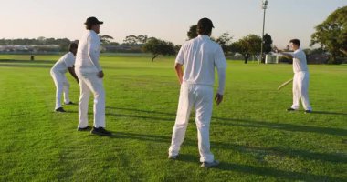 Bowling oyuncusu kırmızı kriket topunu kaldırıyor. Atış talimine başlıyor. Farklı erkek takımlar dış sahada. Spor, takım çalışması, antrenman, eğlence, atletik, dayanıklılık, açık hava