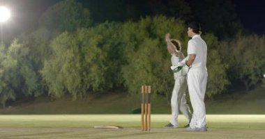 Hakem kararından sonra temyize giden erkek takım arkadaşları gece bekçilik yapan topallara tezahürat yapıyor. Kriket, kutlama, takım çalışması, gece, spor, atletizm, rekabetçilik