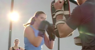 Antrenör, eldivenli, mavi elbiseli bir bayan stajyer ile jimnastik salonunda eldiven geliştirme hızında kombinasyonlar yapıyor. Boks, fitness, antrenman, spor, atletik, hareket, aksiyon