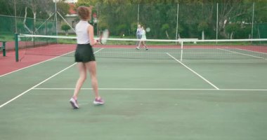 Arkadaşlarıyla miting düzenliyor, kahverengi saçlı kadın top atıyor, sert kortta forehand vuruyor. Açık hava, spor, takım çalışması, fitness, eğlence, enerjik, atletik