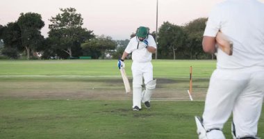 Cırcır böceği erkek takım arkadaşlarının alacakaranlıkta kriket sahasında kırışıp kırışmalarına tepki veriyor. Kriket, sportmenlik, atletizm, takım çalışması, açık hava, alacakaranlık, yarışma