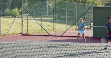 Darbe partneri sarı topu el altından yolluyor, çeşitli arkadaşlar parktaki kortta raketlerle ter döküyor. Spor, eğlence, açık hava, aktif giysi, takım çalışması, eğlence, canlı