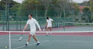 Gevşek tenis toplarını topluyor, erkek tenis partnerleri servis yapıyor ve dışarıda voleybol oynuyorlar. Atletizm, rekabet, takım çalışması, spor, aktif, eğlence, açık hava