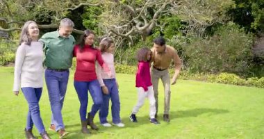 Aile, ağacın altında çimlerde dolaşır, diz çöker ve çocuğu omuzlarına kaldırır, portre pozu verir. Aile, açık hava, doğa, eğlence, uyum, birliktelik, gündelik