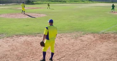 Vurucunun vuruşuna tepki veren üçüncü kaleci, üçüncü kalenin yakınındaki koşucuyu yakalamak için eldiveni hareket ettiriyor. Atletizm, rekabet, sportmenlik, takım çalışması, açık hava, dinamik, aktif giyim