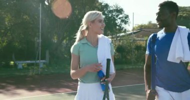 Çeşitli tenis partnerleri sahada hoplayıp zıpladıktan sonra raket dağıtarak ve gülerek yürüyor. Atletik, takım çalışması, eğlence, açık hava, eğlence, canlı, dinamik