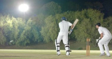 Bovling topu Hint vurucusuna veriyor topa vurmak için sopa sallıyor kaleci topları topluyor. Kriket, spor, gece sporu, atletik, yarışma, aksiyon, takım