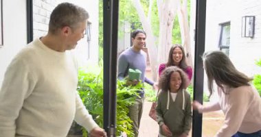 Olgun çift, girişte çift kapı açıyor ve hediye kutusuyla gelen aileyi karşılıyor. Aile, misafirperverlik, karşılama, birleşme, sıcaklık, bağlantı, kutlama