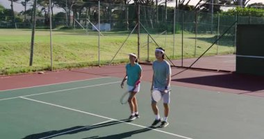 Tenis kortunda raketlerle yürüyen çeşitli takımlar el sıkışıyor ve saygı gösteriyorlar. Atletizm, rekabet, yoldaşlık, açık hava, spor, takım çalışması, zafer