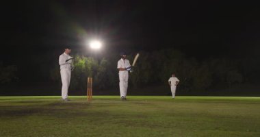 Bowler topu teslim ediyor, Hintli erkek vurucu atış yapıyor ve projektörlerin altında kararını bekliyor. Kriket, spor, yarışma, gece yarısı, atletik, aksiyon, takım