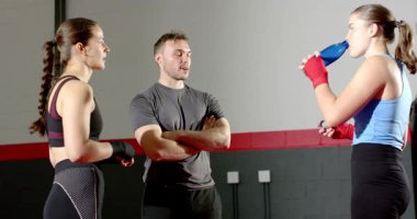 Antrenmandan sonra, koç geri bildirim veriyor, bayan stajyerler su şişelerini yudumluyor jimnastik salonunda sargılarını düzeltiyorlar. Eğitim, motivasyon, dayanıklılık, fitness, disiplin, dinamik, azim