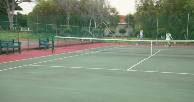 Top servisi yaptıktan sonra, bayan arkadaşlar tenis kortunun yanında tenis topları atıyorlar, fotokopi alanı. Açık hava, eğlence, aktivite, spor, arkadaşlık, atletik, gündelik