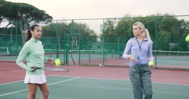 Çeşitli bayan antrenörler ve öğrenciler Red Hartcourt 'ta ısınmak için top atıp raket sallıyorlar. Koçluk, antrenman, atletik, aktif, takım çalışması, spor giyimi