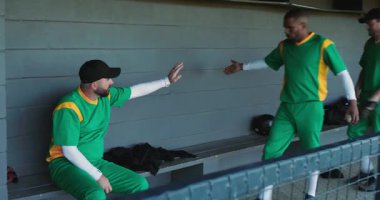 Çeşitli erkek beyzbol oyuncuları yedek kulübesinde takım arkadaşlarıyla el sıkışıyor ve maç için hazırlanıyor. Takım çalışması, dostluk, sportmenlik, atletizm, odaklanma, gündelik, canlı