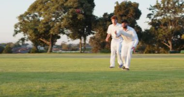 Antrenman sırasında erkek takım arkadaşları dış sahada kriket topunu yakalamak için atış yapar ve dalarlar. Atletizm, takım çalışması, aksiyon, açık hava, enerjik, sportmenlik, dinamik