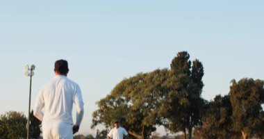 Antrenman yapan Hintli vurucu, atıcı koşarken, beysbol sopasını ters çeviriyor ve saha dalışı yaparken topu yakalıyor. Spor, açık hava, takım çalışması, atletik, aksiyon, antrenman, eğlence