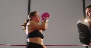 Eğitmen eldiven değiştiriyor, boksör kadın boksörleri teşvik ediyor. Kanca ve ön tekme denemeleri yapıyor. Sporcu, koç, antrenman, güç, teknik, fitness, disiplin