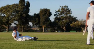 Çeşitli erkek kriket oyuncuları parktaki antrenmanlarda topa vuruyor ve topa vuruyor. Atletik, takım çalışması, açık hava, dinamik, spor, eğlence, rekabet
