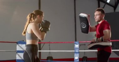 Bayan atlet ve antrenör boks ringinde yumruk-tekme kombinasyonu çalışmasını takip ediyoruz. Eğitim, spor, dövüş, dövüş sanatları, güç, hassasiyet, çeviklik