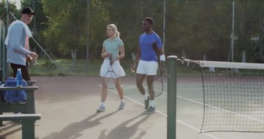 Çeşitli tenis takımları yedek kulübesinde raket tutuyor, içki içiyor ve koçun stratejisini dinliyor. Sporcular, takım çalışması, eğitim, açık hava, enerji, kararlılık, rekabetçi