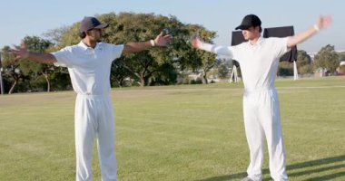 Solun işaretini takip eden çeşitli erkek kriket oyuncuları ısınmak için sahada kol kola giriyorlar. Atletik, takım çalışması, antrenman, açık hava, dinamik, fitness, spor