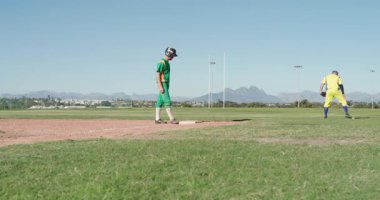 Birinci kalede koşan gözlemci, saha oyuncusu eldiveni ayarlarken koşucu sahada çömeliyor. Atletik, rekabet, spor, takım çalışması, açık hava, dinamik, strateji