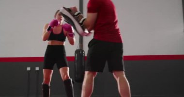 Koç pedleri tutarken, boksör adayı kadın boksör boks ringinde güç için tekme ve yumruk atıyor. Martialart, fitness, eğitim, güç, disiplin, dinamik, atletik