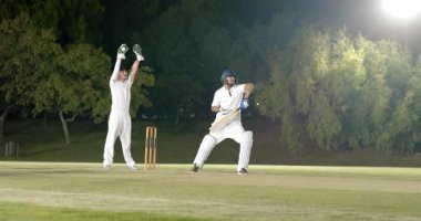 Bowler, şaşkın sahada top dağıtıyor. Hintli vurucu, top tutucuyu hokkabazlık yaparken yakalıyor. Kriket, gece, spor, yarışma, atletizm, stadyum, takım çalışması
