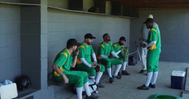 Yedek kulübesinde eldiven ve miğferlerle maça hazırlanan çeşitli beyzbol takımları geliyor. Atletik, takım ruhu, takım çalışması, spor giyim, açık hava, rekabetçi, enerjik