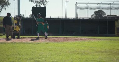 Atış vurucusu yeşil üniformalı, kale levhasından vuruyor, ilk kaleye ulaşmak için koşuyor. Sporcu, müsabaka, atletizm, açık hava, hareket, takım, disiplin