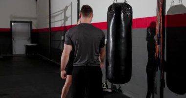 Erkek antrenör kum torbasına hafifçe vuruyor ve kadın stajyer boks salonunda zamanlama talimi için yumruk atıyor. Eğitim, antrenman, dövüş, spor, güç, atletik, disiplin