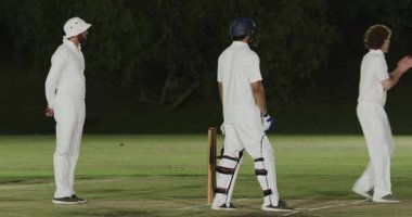 Bowlingci vurucuya bakıyor, çeşitli erkek kriketçiler koşuyor, atış alanına meydan okuyor. Atletizm, takım çalışması, rekabet, açık hava, spor, gece, aksiyon