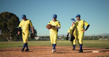 Üniformalı dört yetişkin adam sahadan sahaya doğru yürüyorlar ve eldiven taşıyorlar. Atletizm, takım çalışması, dostluk, sportmenlik, boş zaman, açık hava, güneş ışığı.