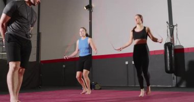 Antrenör, iki bayan stajyerin atlama iplerini kesmesi ve spor salonunda göğüs germeye başlaması için işaret veriyor. Spor, egzersiz, egzersiz, egzersiz, kardiyo, güç, sağlık