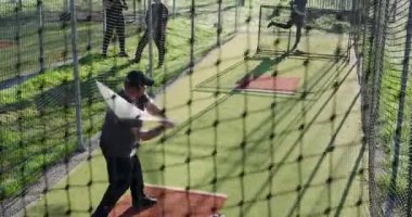 Yetişkin bir erkek vurucu antrenman için vuruş kafesinde sopa sallıyor. Atletik, takım çalışması, antrenman, spor, koçluk, açık hava, kararlı