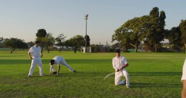 Çeşitli erkek oyuncular teslimatta sopayı sallıyor, topu alıyor, sahada koşular için uçlarını değiştiriyor. Kriket, atletizm, takım çalışması, sportmenlik, açık hava, enerjik, rekabetçi