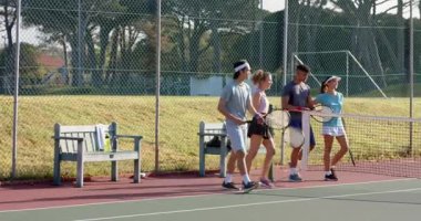 Banklarda dikilen, çeşitli arkadaşlar sahada volta atıyor, raketleri birbirine vuruyor. Açık hava, eğlence, atletik, arkadaşlık, takım çalışması, canlı, enerjik